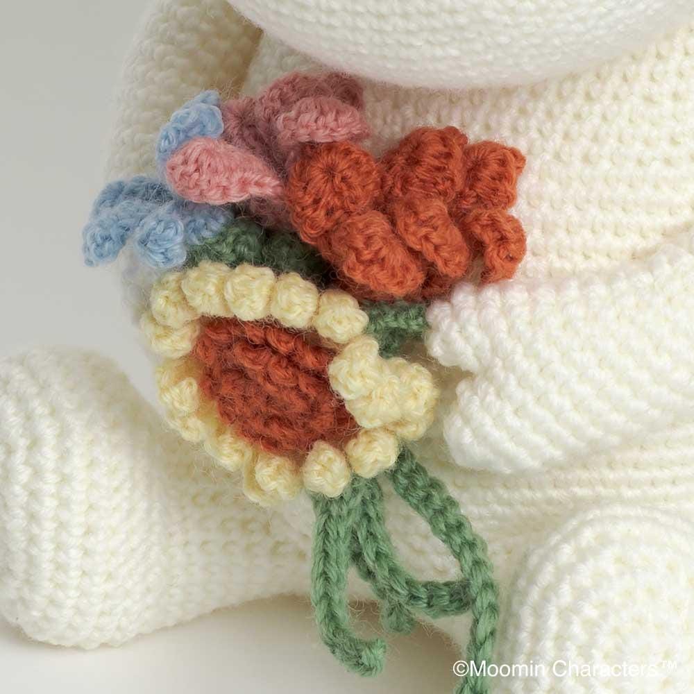 A close-up image of a crocheted flower in a white fabric, with a green stem and yellow petals.