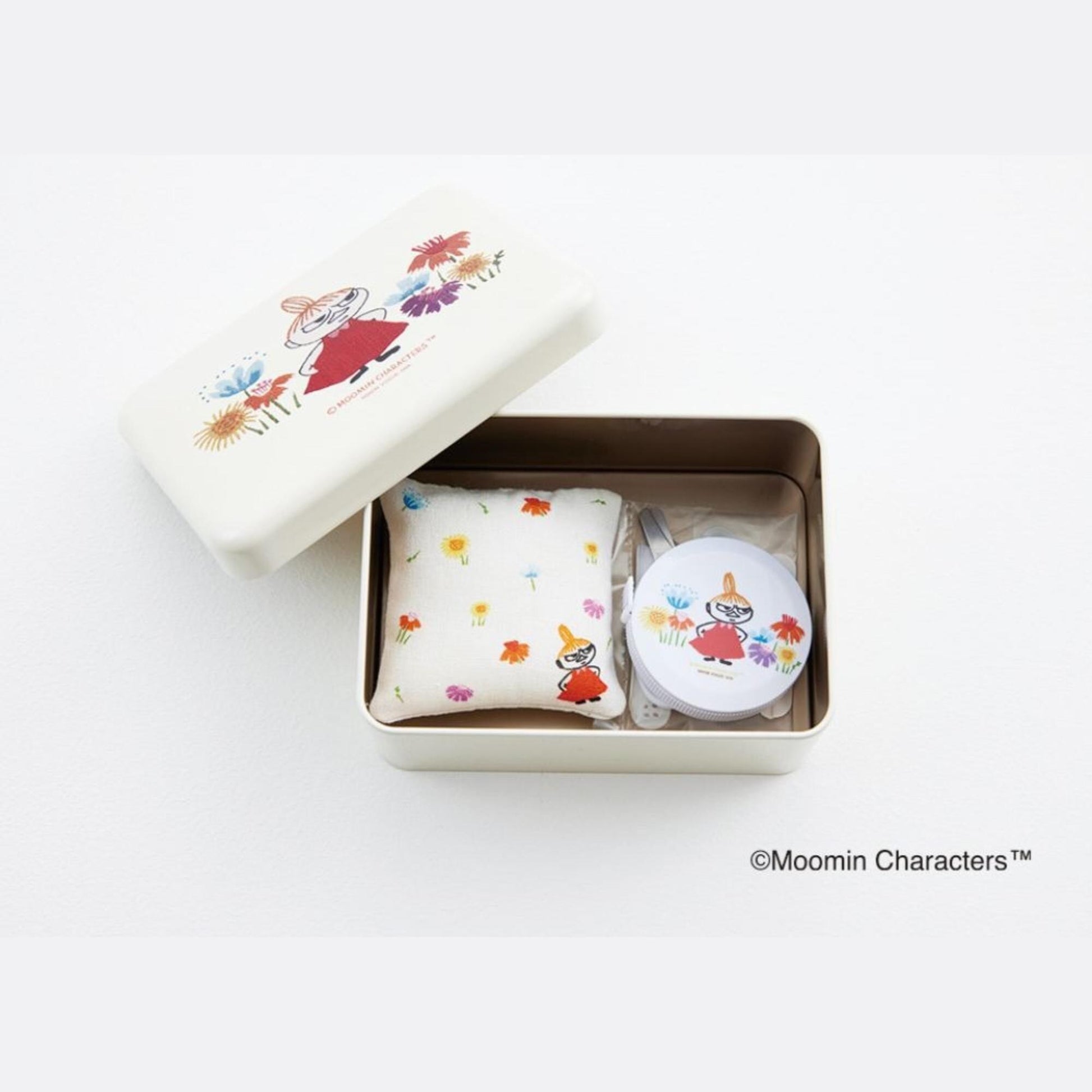 A white box containing a small white pillow with colorful flowers and a round white object with a similar design.