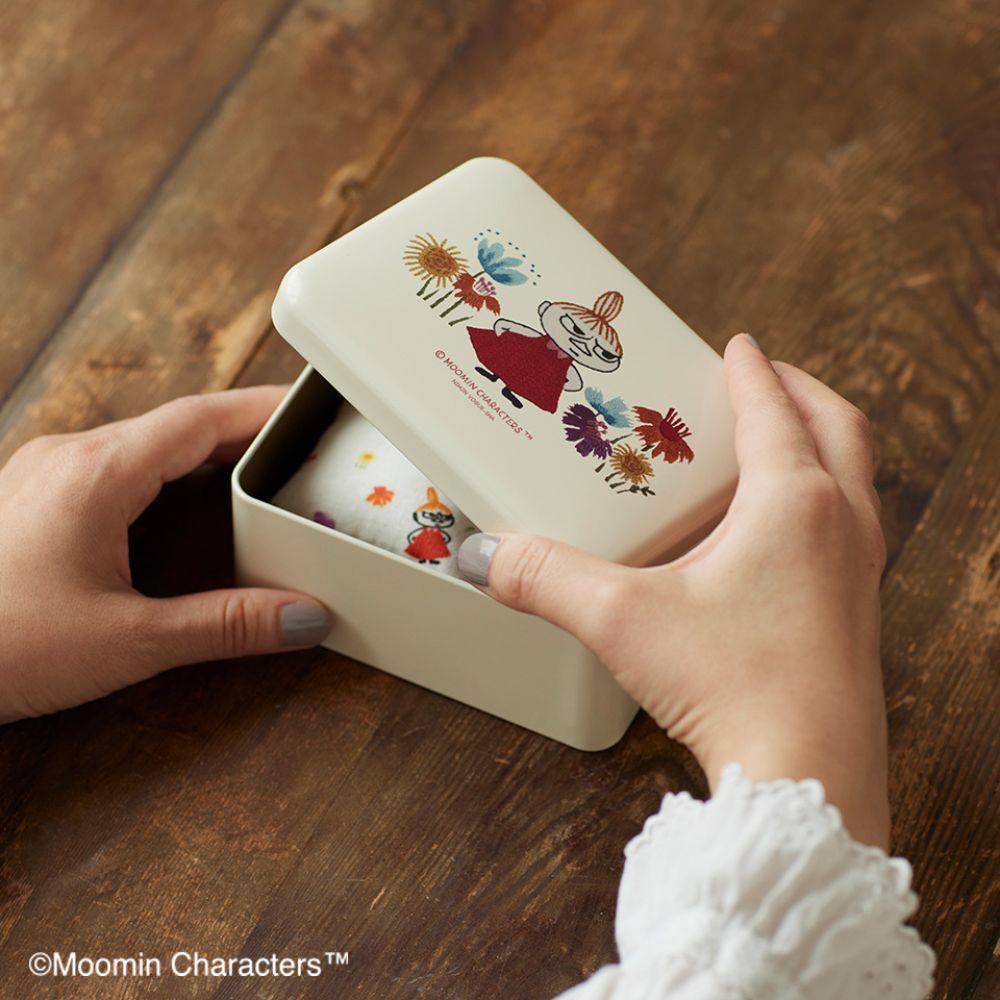 A person's hands are holding a white box with a colorful illustration of a character on it, placed on a wooden surface.