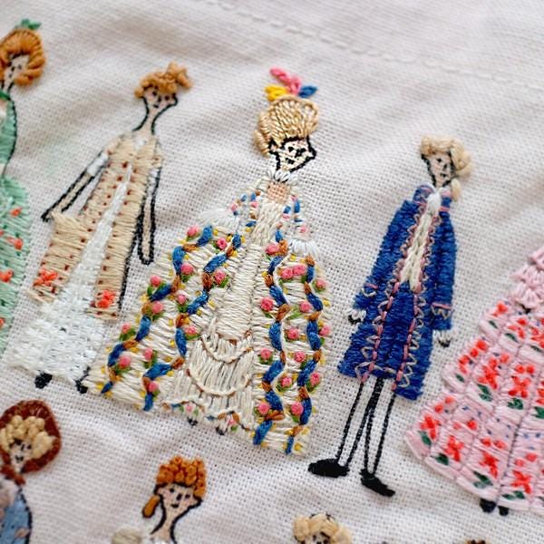 a close-up view of a hand-embroidered scene with various stylized figures wearing elaborate, colorful dresses.