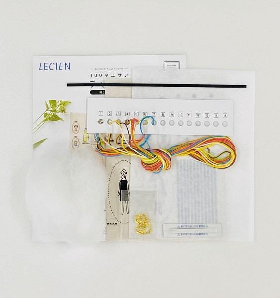 various objects, including a piece of paper with instructions, a spool of thread, and some other items, all arranged on a white background.
