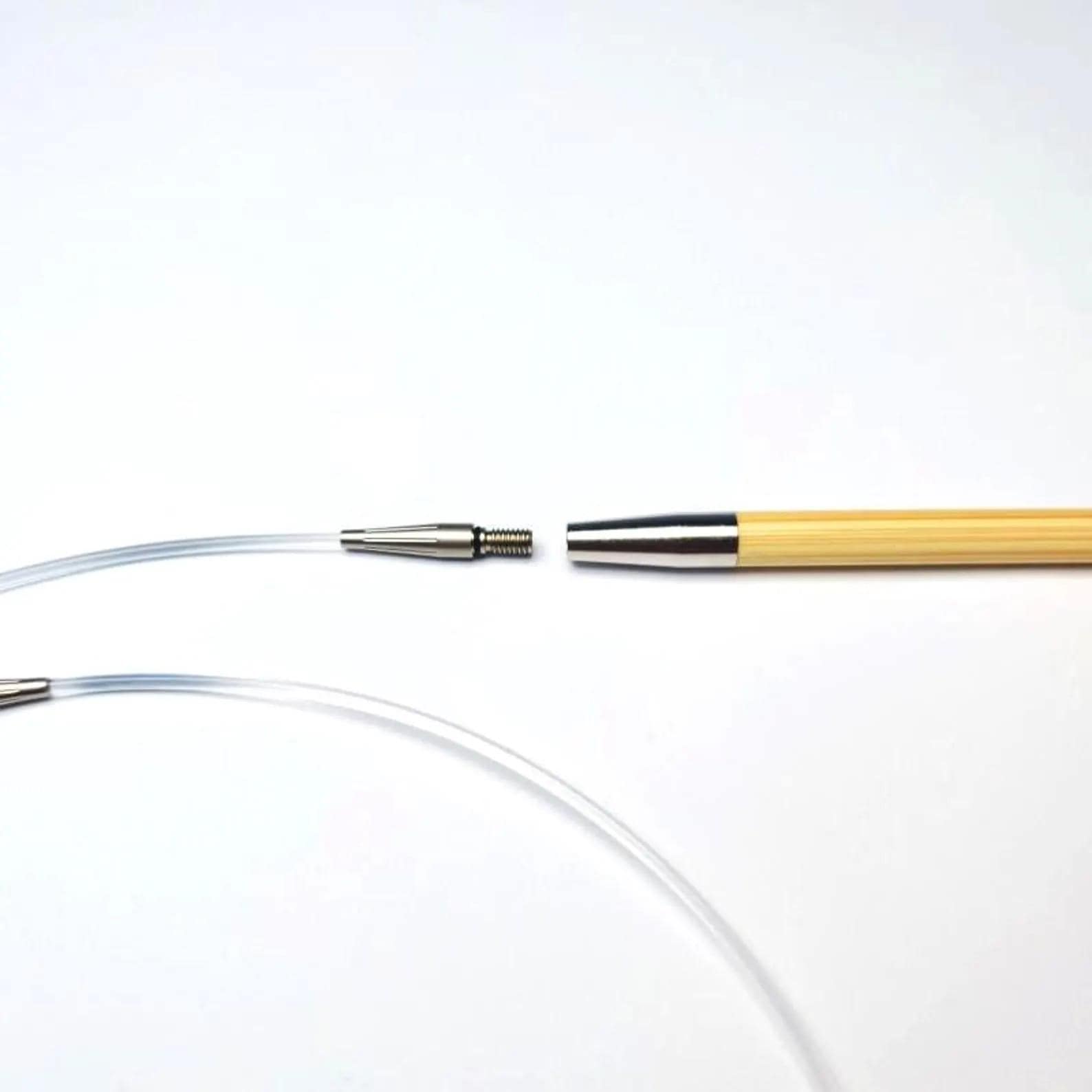 a clear plastic tube and a wooden knitting needle with a silver connector, both lying on a white surface.