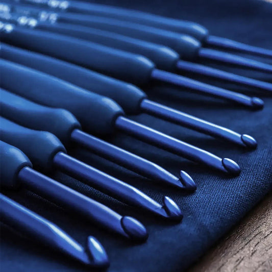 A close-up view of a collection of blue crochet hooks arranged in a row on a dark blue surface.