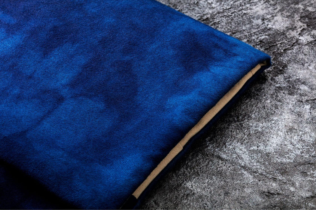 A close-up view of a blue fabric, possibly a blanket or cushion, resting on a textured gray surface.