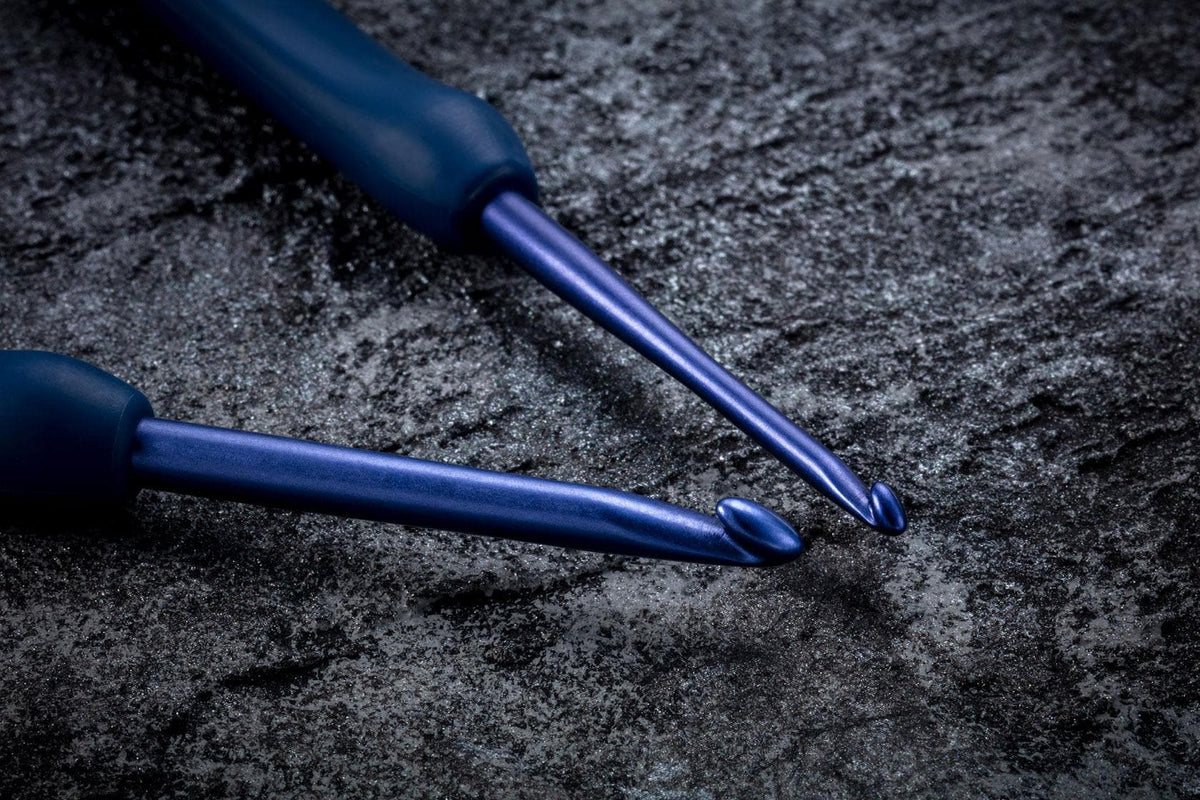 Two blue crochet hooks lying on a textured surface.