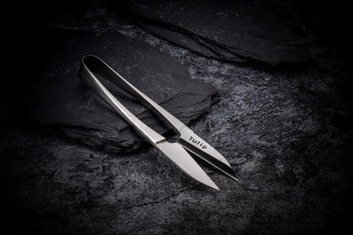 A pair of silver scissors rests on a dark surface, with the brand name "TULIP" visible on the blades.