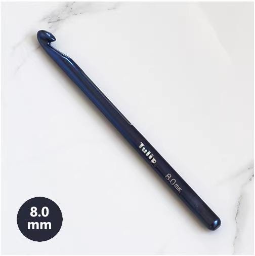 A blue crochet hook with the text "Tulip" printed on it, lying on a white marble surface.