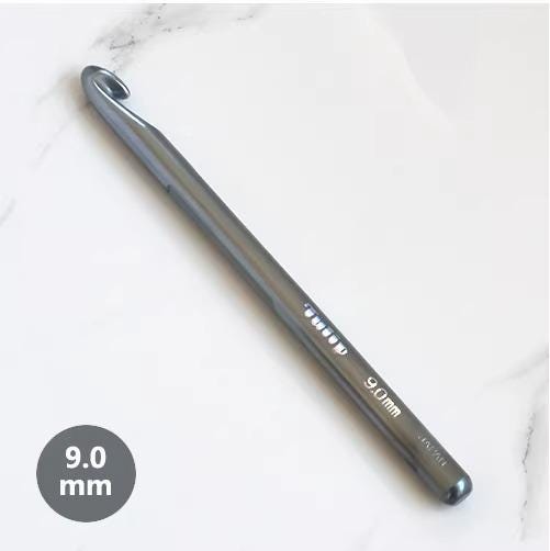 A crochet hook with a silver or grey color is lying on a white marble surface.