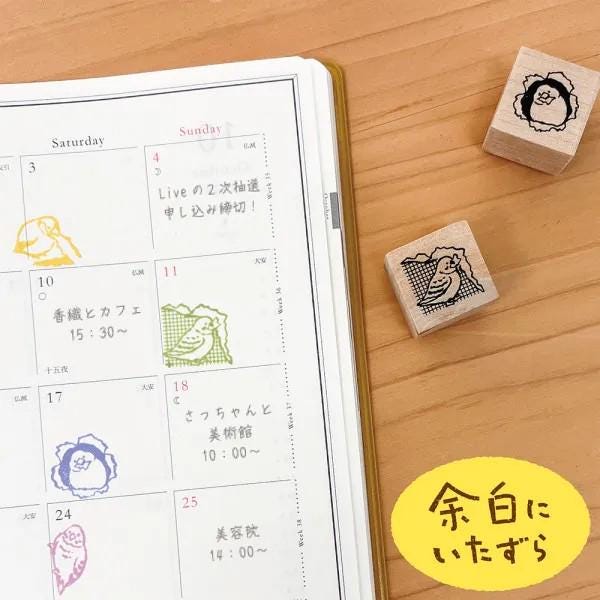 a calendar with a yellow border, a yellow sticky note, and three wooden stamps with Japanese characters on a wooden surface.