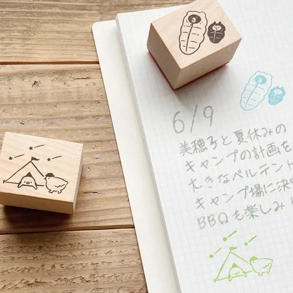 a wooden stamp with a cartoon image and a handwritten note on a notebook with Japanese text.