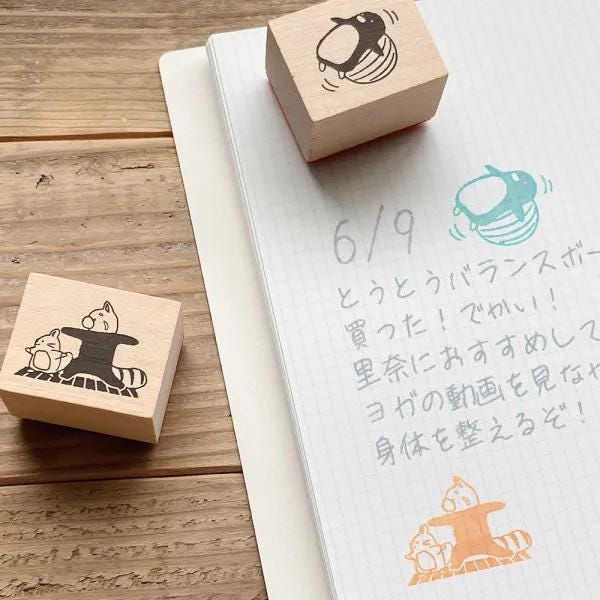 a wooden stamp with a cat design and a handwritten note on a notebook with Japanese text.