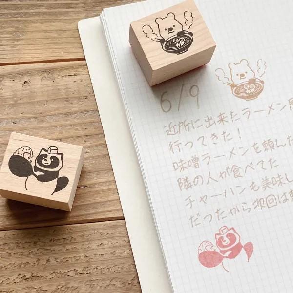 a wooden stamp with a cat design and a handwritten note on a notebook with Japanese text.