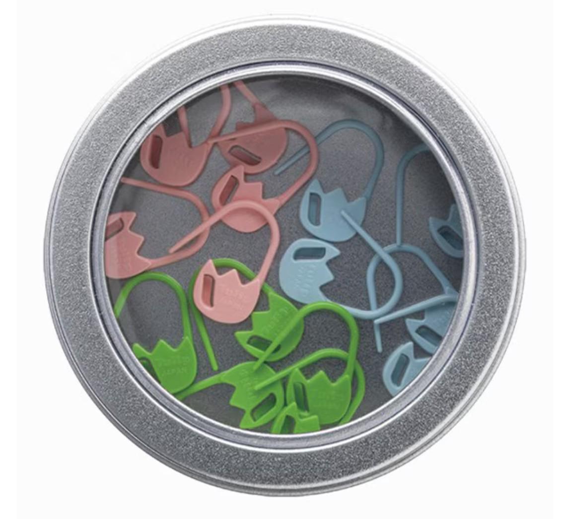 A silver tin can containing a collection of colorful plastic sewing needles in various colors, including pink, green, and blue.
