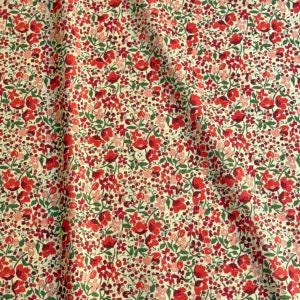 a close-up view of a fabric with a floral pattern of red flowers and green leaves. The fabric appears to be a light-colored material, possibly beige or cream, with a textured and wrinkled appearance.