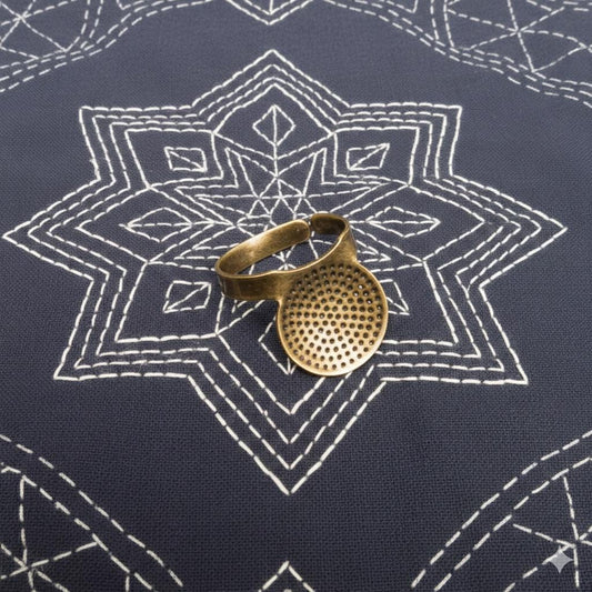A brass ring with a perforated design rests on a dark blue fabric with a white star-shaped pattern.