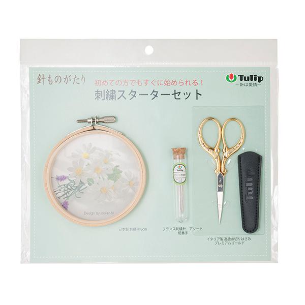 a package containing a sewing kit with a circular embroidery hoop, a pair of gold scissors, and a small glass bottle with a label.