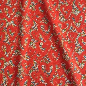 a close-up view of a fabric with a floral pattern in shades of red and white. The fabric appears to be made of a soft, textured material, and there is a small button visible in the center of the pattern.