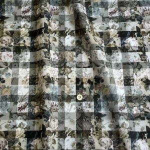 The image is a close-up of a fabric with a floral pattern, featuring a variety of flowers and leaves in different shades of green, black, and gray. The fabric appears to be a checkered or square pattern, with a button visible in the center.