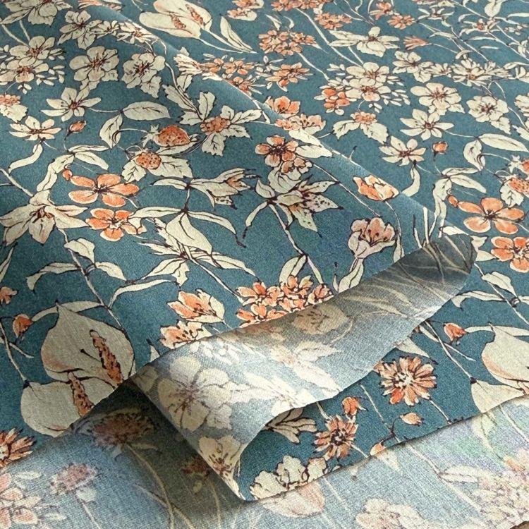 a close-up view of a fabric with a floral pattern in shades of blue and orange. The fabric appears to be folded or rolled, revealing the intricate design of the flowers and leaves.