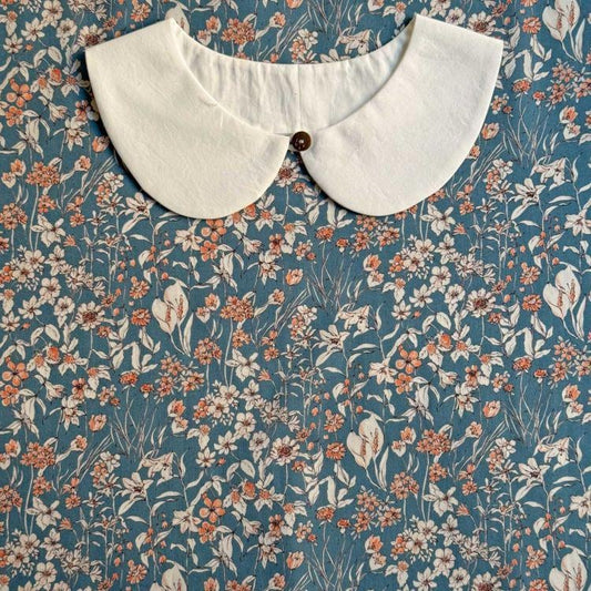 a white collar with a button, set against a blue floral print background.
