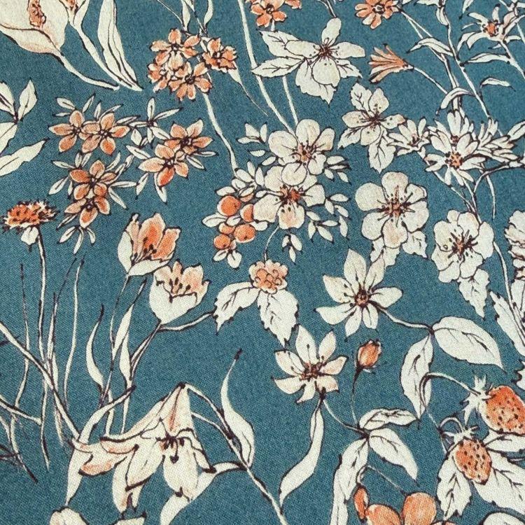 a close-up view of a fabric with a floral pattern. The fabric has a blue background with white and orange flowers and leaves, creating a visually appealing and vibrant design.