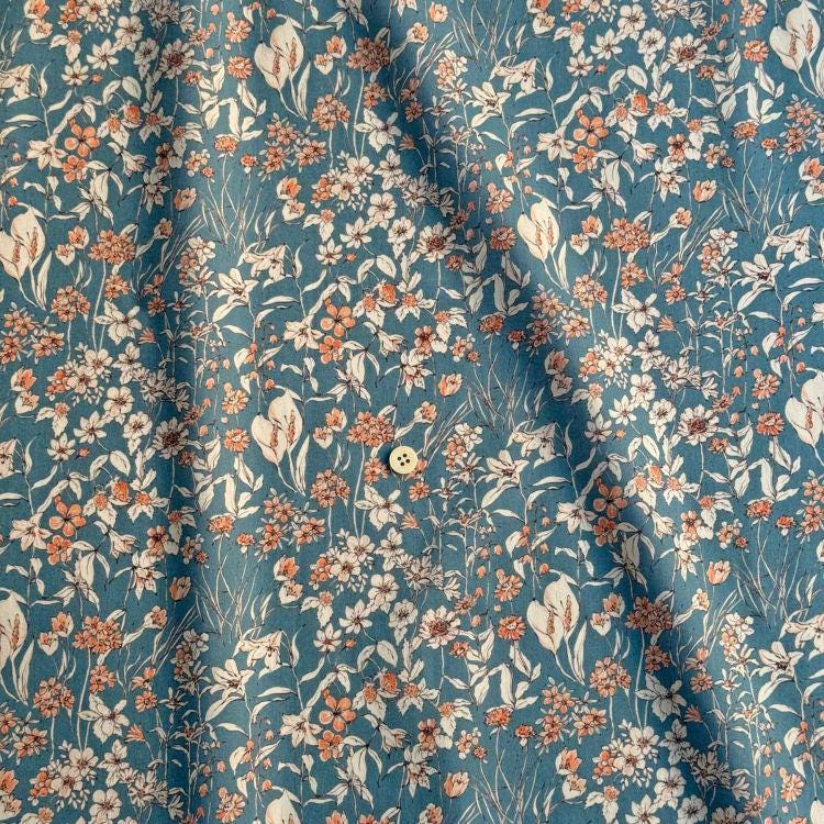 a close-up view of a fabric with a floral pattern in shades of blue and orange. The fabric appears to be made of a soft, textured material, and there is a small button visible in the center of the pattern.