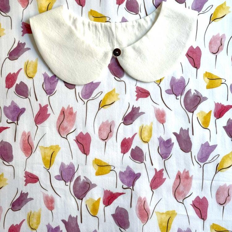 a white collar with a button, set against a background with a repeating pattern of colorful tulips in shades of pink, yellow, and purple.