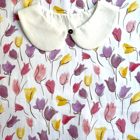 a white collar with a button, set against a background with a repeating pattern of colorful tulips in shades of pink, yellow, and purple.