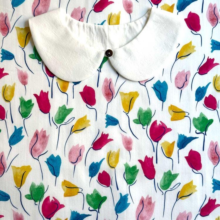 a white collar with a button, set against a background with a repeating pattern of colorful flowers in various shades of pink, yellow, green, and blue.