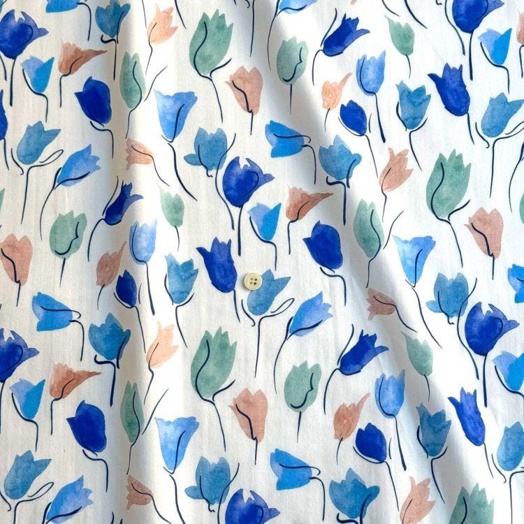 a close-up view of a fabric with a repeating pattern of blue and green watercolor flowers.