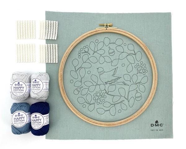a sewing kit containing various supplies, including embroidery floss, yarn, and a hoop for embroidery. The kit appears to be a kit for creating a floral design on a canvas or fabric.