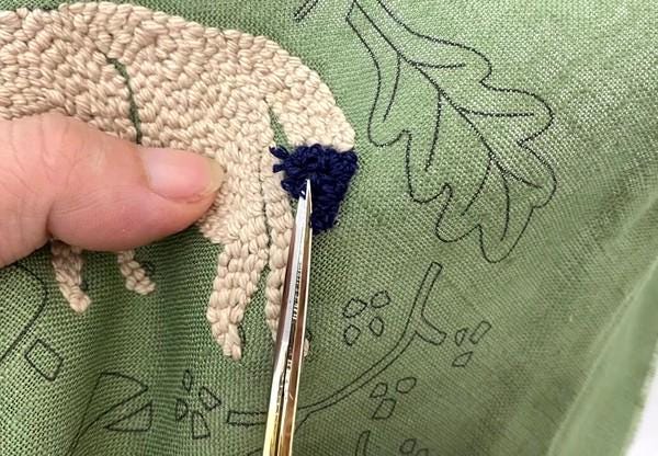 A hand is holding a pair of scissors and cutting a piece of fabric with a blue and beige design.