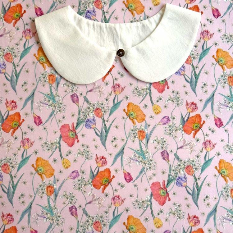 a white collar with a button, placed on a pink floral background with various colorful flowers and leaves.