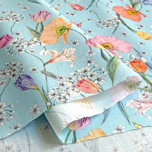 a close-up view of a fabric with a vibrant floral pattern. The fabric is predominantly blue, with various flowers such as tulips, lilies, and daisies in shades of pink, orange, and white. The flowers are arranged in a way that creates a visually appealing and colorful design.