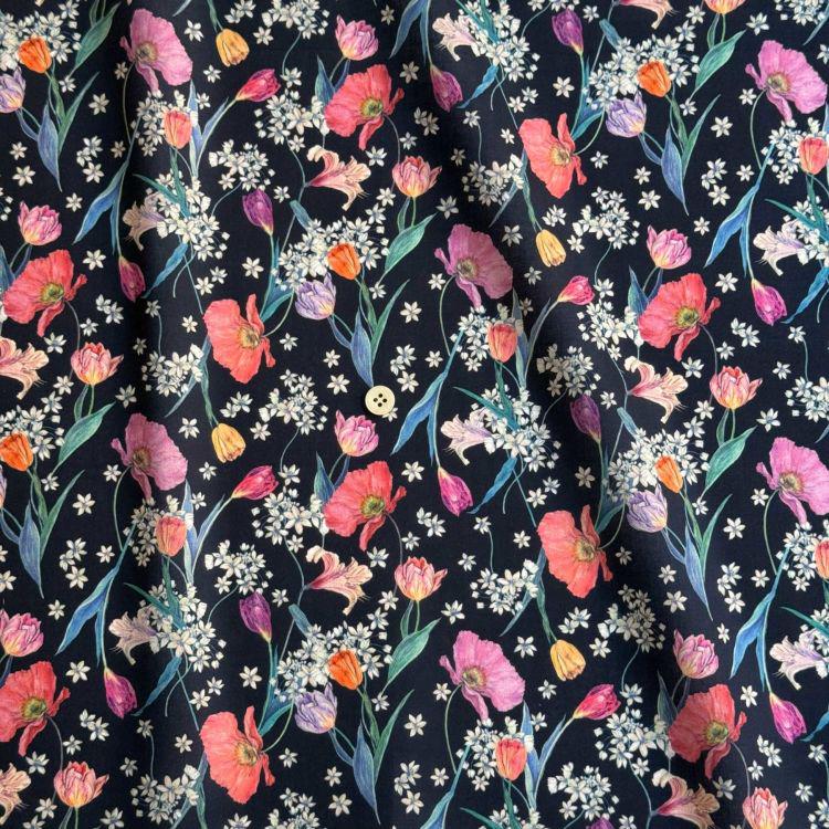 a close-up view of a fabric with a floral pattern. The fabric is predominantly black, adorned with a variety of colorful flowers and leaves, including red, pink, orange, and purple flowers, as well as green leaves. The flowers are scattered throughout the fabric, creating a vibrant and lively visual effect. The fabric appears to be a dark-colored material, possibly cotton or a similar type of fabric.