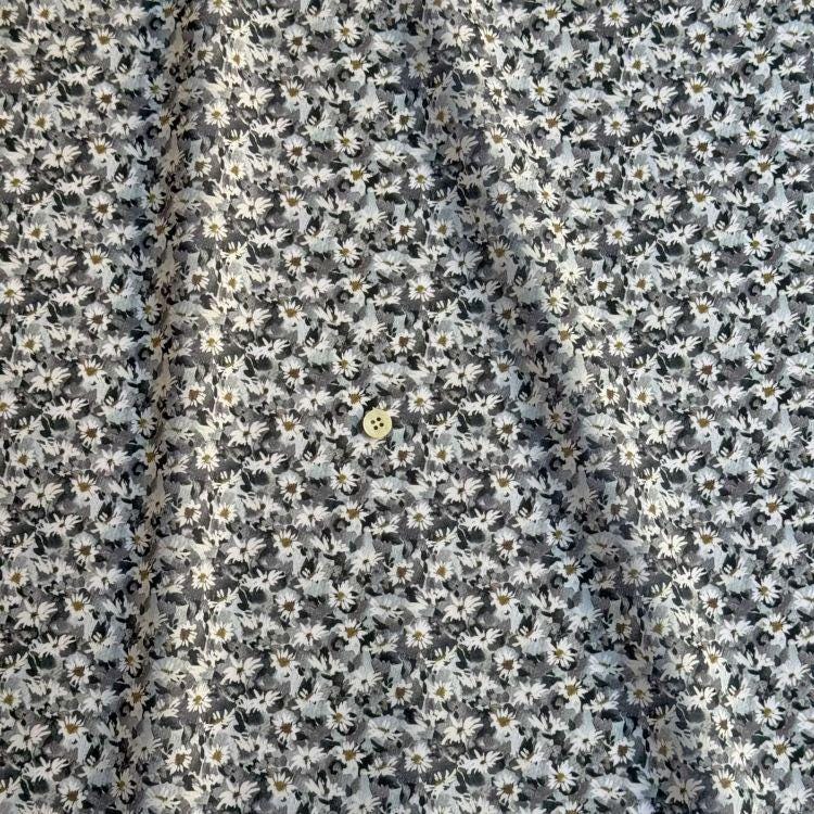 a close-up view of a fabric with a grey and white floral pattern. The fabric appears to be made of a material with a subtle texture, and there is a small button visible in the center of the fabric.