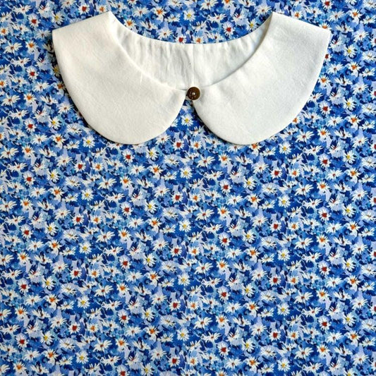 a white collar with a button, set against a background of a blue floral print fabric.