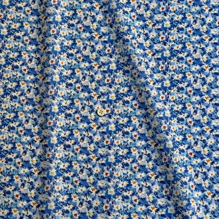 a close-up view of a fabric with a blue floral pattern. The fabric appears to be made of a soft, flowy material, and there is a small white button visible in the center of the fabric.