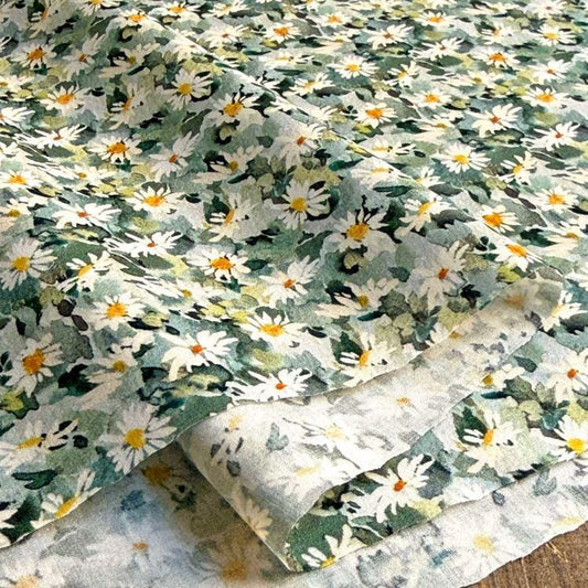 a close-up view of a fabric with a floral pattern, predominantly consisting of white and green flowers. The fabric appears to be a piece of cloth or textile, with the flowers arranged in a repeating pattern across the surface.