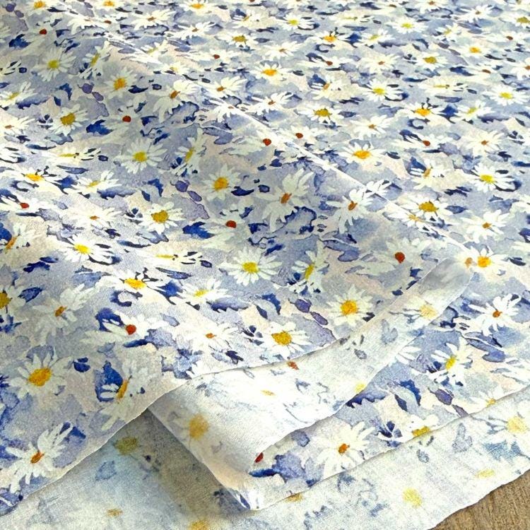 a close-up view of a fabric with a floral pattern, featuring white and blue flowers. The fabric appears to be folded or rolled, creating a textured and visually appealing design.