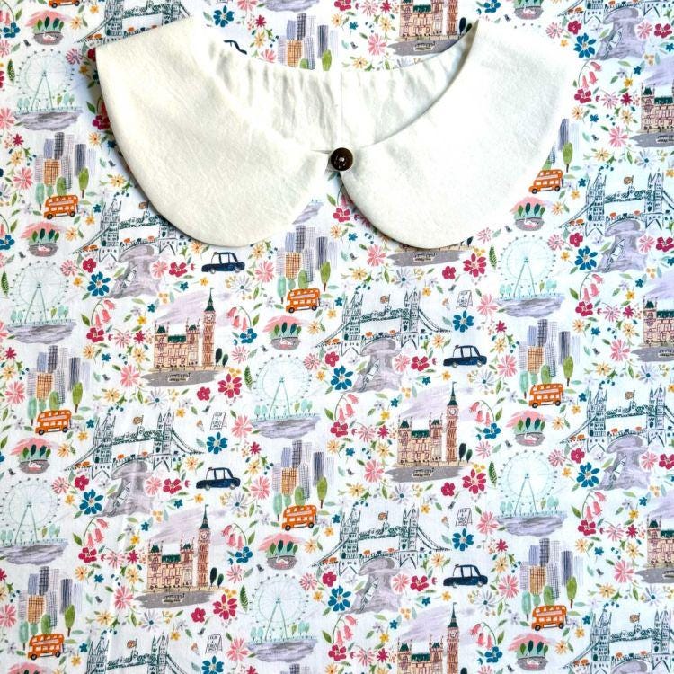 a white collar with a button, set against a background with a repeating pattern of various city landmarks and scenes, including a ferris wheel, buildings, and vehicles.