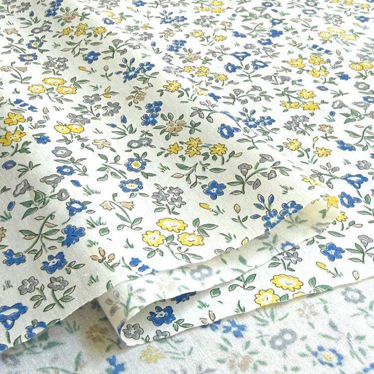 a close-up view of a fabric with a floral pattern in shades of blue, yellow, and white. The fabric appears to be folded or rolled, revealing the intricate design of the flowers and leaves.