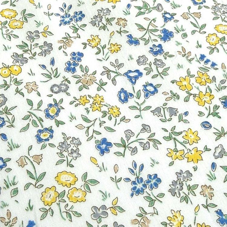 The image is a close-up of a white fabric with a floral pattern of various colored flowers, including yellow, blue, and gray.
