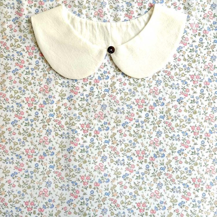 a white collar with a button, set against a background of a floral print fabric.