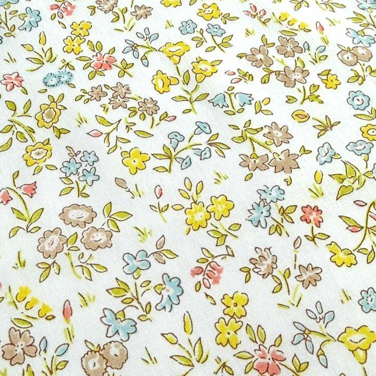 The image is a close-up of a white fabric with a floral pattern. The pattern consists of various types of flowers, including daisies, roses, and other colorful blooms, arranged in a visually appealing manner. The flowers are depicted in different sizes and orientations, creating a dynamic and lively design. The fabric appears to be a soft, delicate material, suitable for clothing or home decor.