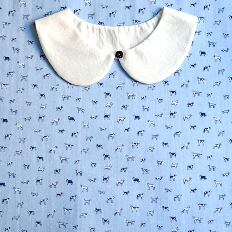 a white collar with a button, placed on a blue fabric with a repeating pattern of small white dogs.