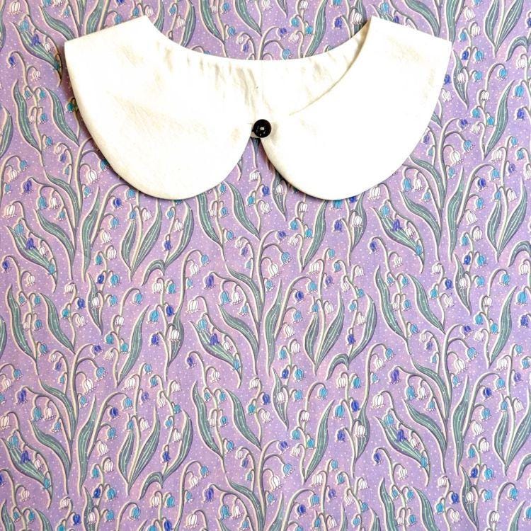 a white collar with a black button, set against a background with a floral pattern in shades of purple and blue.