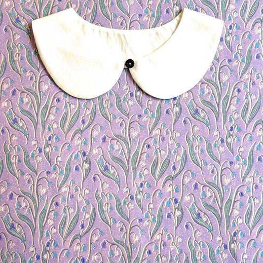 a white collar with a black button, set against a background with a floral pattern in shades of purple and blue.
