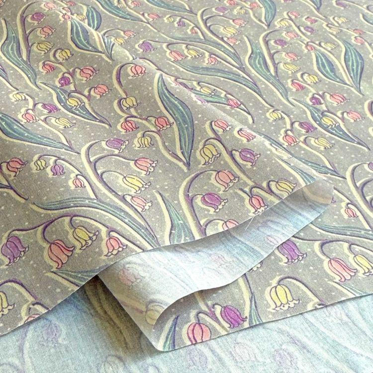 a close-up view of a fabric with a repeating pattern of colorful flowers and leaves, including lily of the valley flowers.