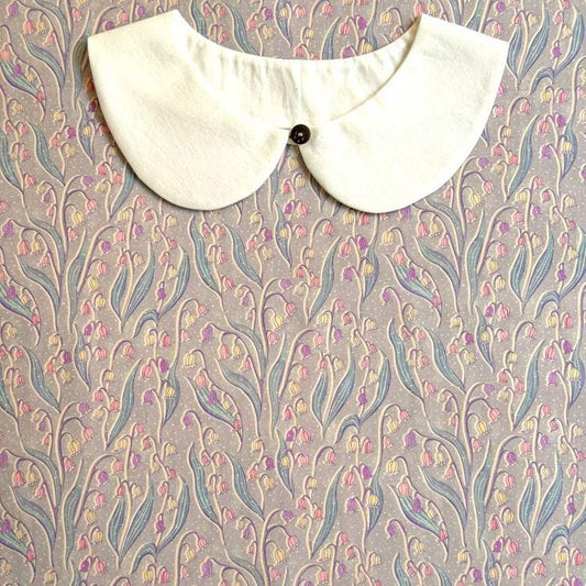 a white collar with a button, placed on a patterned fabric with a floral design.